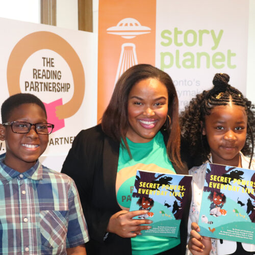 Camesha Cox stands with a young boy and girl. They’re holding a copy of our anthology, titled “Secret Powers, Everyday Lives.”