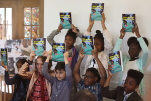 A group of kids ages 9 to 12 hold up copies of an anthology that holds their work as newly published authors.