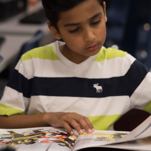 A young boy sits at a table reading a children’s book.