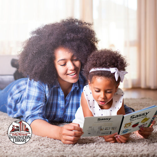 A mother and her young daughter lay on the floor, reading a children’s book.